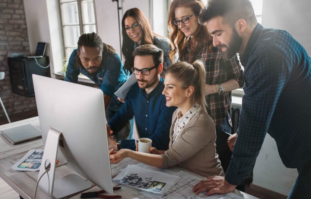 A diverse team of colleagues collaborating around a computer in a modern office.