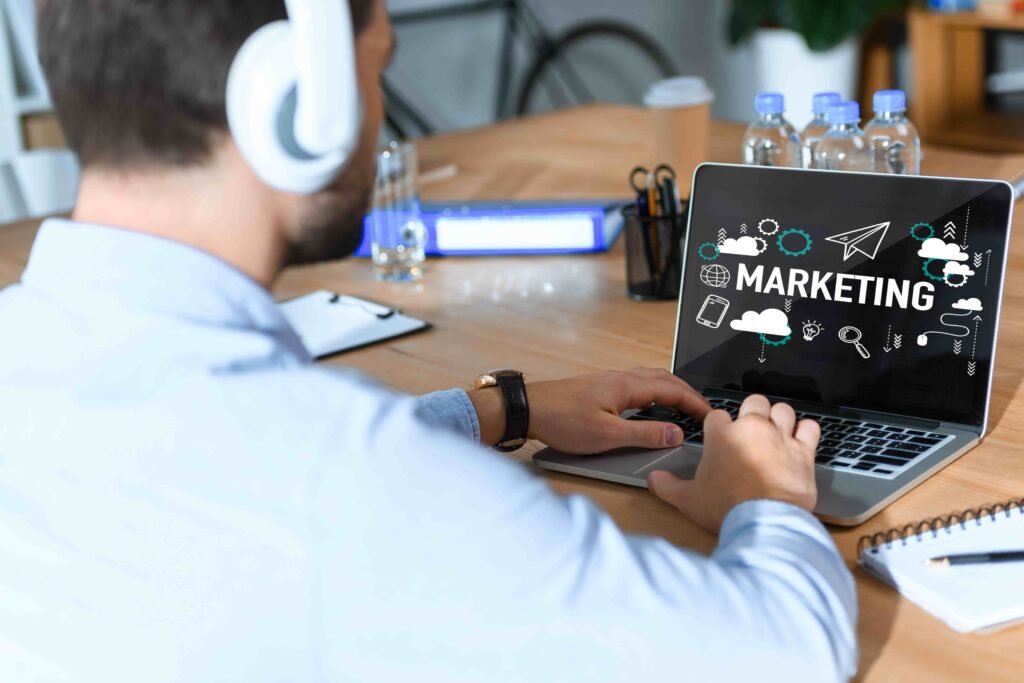 A man in headphones works on a laptop with "Marketing" displayed. - Marketing and Digital Marketing Services