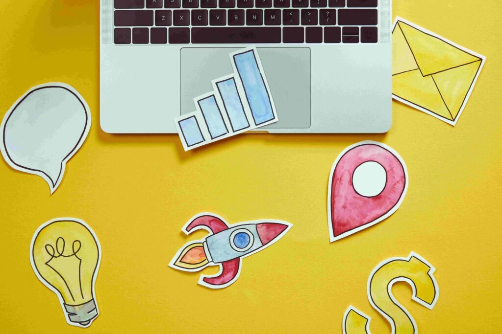 Laptop with colorful paper cutouts on a yellow background. - best digital marketing company in Kochi